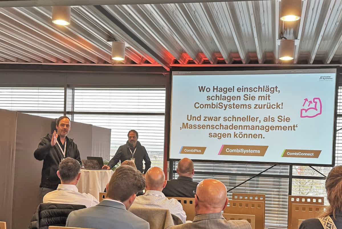 Stefan und Sebastian Grimm von CombiSystems präsentieren auf dem HagelCampus 2025. Vor ihnen sitzt ein interessiertes Publikum. Auf der großen Leinwand steht: „Wo Hagel einschlägt, schlagen Sie mit CombiSystems zurück! Und zwar schneller, als Sie ‚Massenschadenmanagement‘ sagen können.“ Die Produkte CombiPlus, CombiSystems und CombiConnect sind unten hervorgehoben. Die Stimmung ist engagiert und zukunftsorientiert.