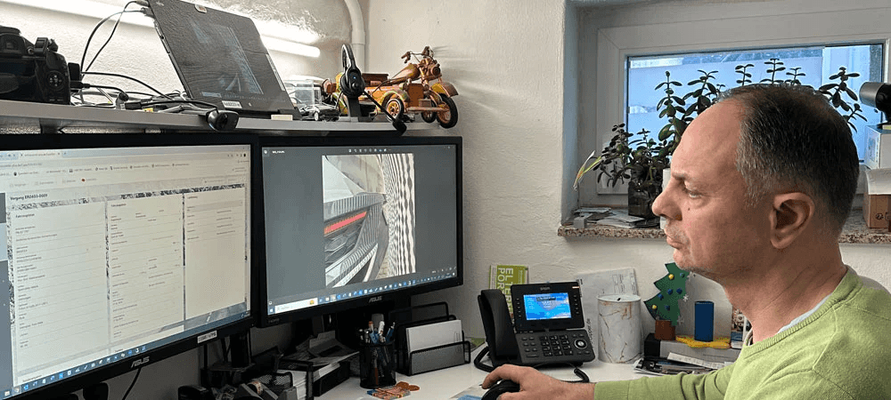 Enrico Rehberg, ein CombiKunde, arbeitet konzentriert an einem Schreibtisch mit zwei Monitoren. Auf den Bildschirmen sind Schadenfotos und Eingabemasken eines digitalen Kfz-Schadenmanagementsystems zu sehen – ein moderner Arbeitsplatz im Sachverständigenwesen.