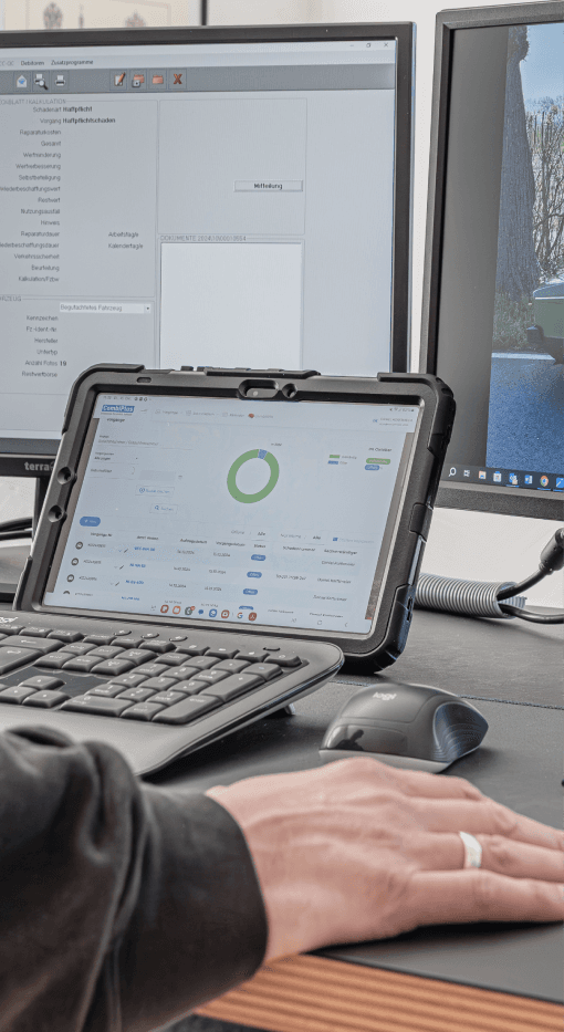 Das Bild zeigt einen Kfz-Sachverständigen, der mit CombiPlus Hybrid arbeitet, um die Vorteile sowohl der CombiPlus Online als auch der CombiPlus Professional Software zu nutzen. Der linke Bildschirm zeigt die Benutzeroberfläche von CombiPlus Professional, die für eine umfangreiche Büroarbeit und detaillierte Schadenbearbeitung verwendet wird. Das Tablet zeigt hingegen die mobile Version, die eine schnelle und flexible Schadenaufnahme vor Ort ermöglicht. Mit CombiPlus Hybrid kombiniert der Sachverständige die Effizienz der mobilen Schadenaufnahme mit den umfassenden Funktionen der Bürosoftware, um eine nahtlose und schnelle Bearbeitung von Schadenfällen zu gewährleisten.