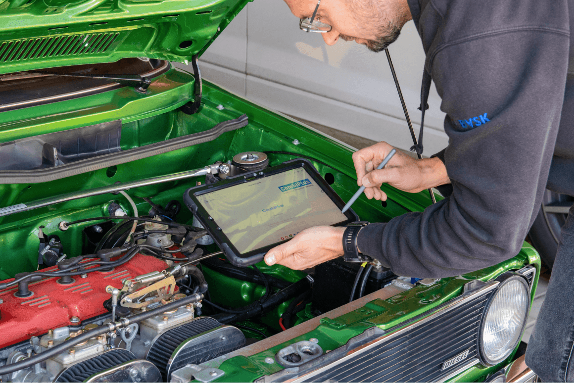 Ein Kfz-Sachverständiger hält ein Tablet und mit einem Stift auf dem Bildschirm schreibt. Er steht vor einem Fahrzeug. Auf dem Tablet ist die Software für Kfz-Sachverständige CombiPlus Online - die mobile Software zur Schadensbearbeitung oder Fahrzeugbewertung.