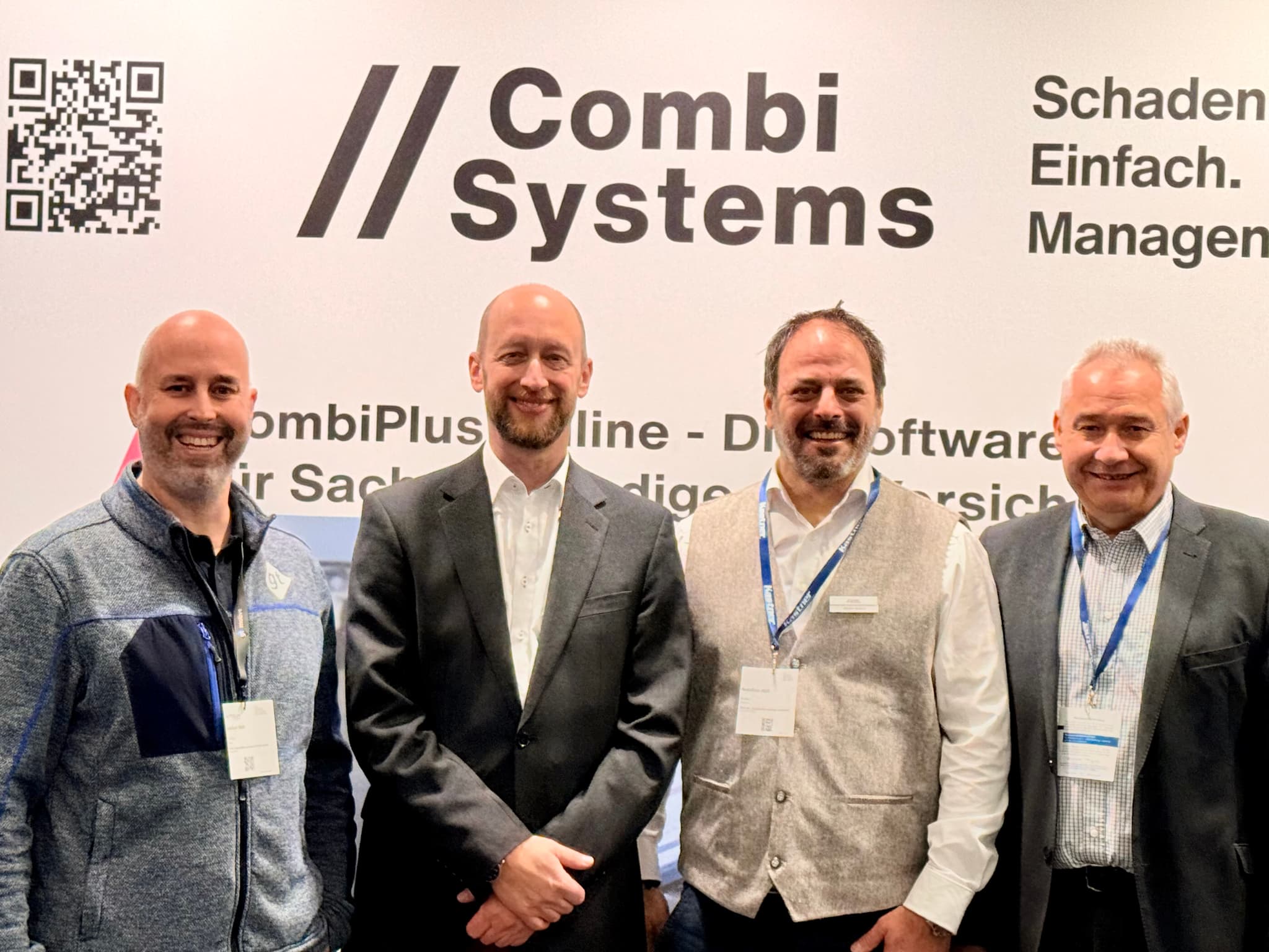 Vier Männer stehen nebeneinander vor einem Messestand auf der AutoZum in Salzburg, wo CombiSystems seine Software für Kfz-Schadenmanagement präsentiert. Der zweite Mann von rechts, Stefan Grimm, Geschäftsführer von CombiSystems, trägt eine traditionelle Weste und ein Namensschild. Im Hintergrund ist das Logo von CombiSystems mit dem Slogan 'Schadenmanagement. Einfach. Management.' sowie ein QR-Code zu sehen.