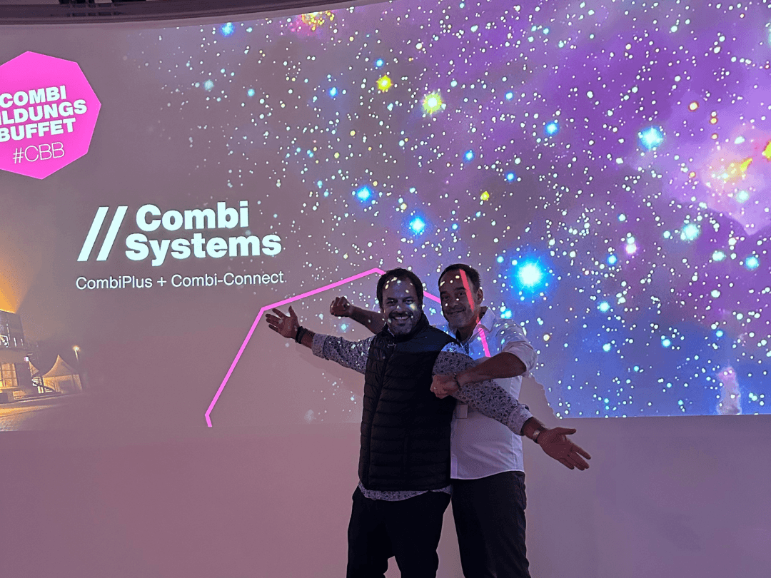 Stefan Grimm und Sebastian Grimm stehen lachend vor einer großflächigen Projektion mit dem Schriftzug 'Combi Systems' und 'CombiPlus + Combi-Connect'. Die Projektion zeigt einen Sternenhimmel in bunten Farben. Beide haben ihre Arme ausgebreitet und freuen sich über die gelungene Veranstaltung des CombiBildungsBuffets.