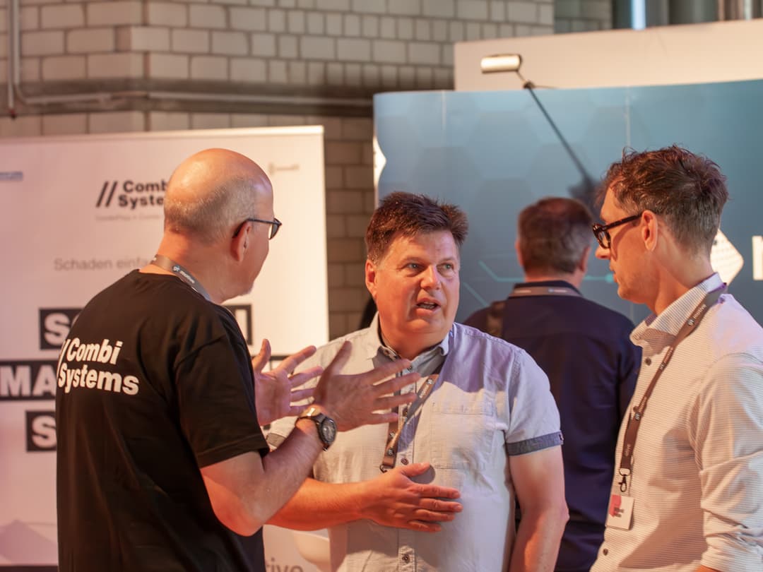 Das Bild zeigt ein intensives Fachgespräch auf dem CombiBildungsBuffet. Teilnehmer diskutieren engagiert über branchenspezifische Themen in einer Networking-Atmosphäre. Im Hintergrund sind Messe- oder Präsentationsstände zu sehen, die auf die Fachveranstaltung hinweisen.