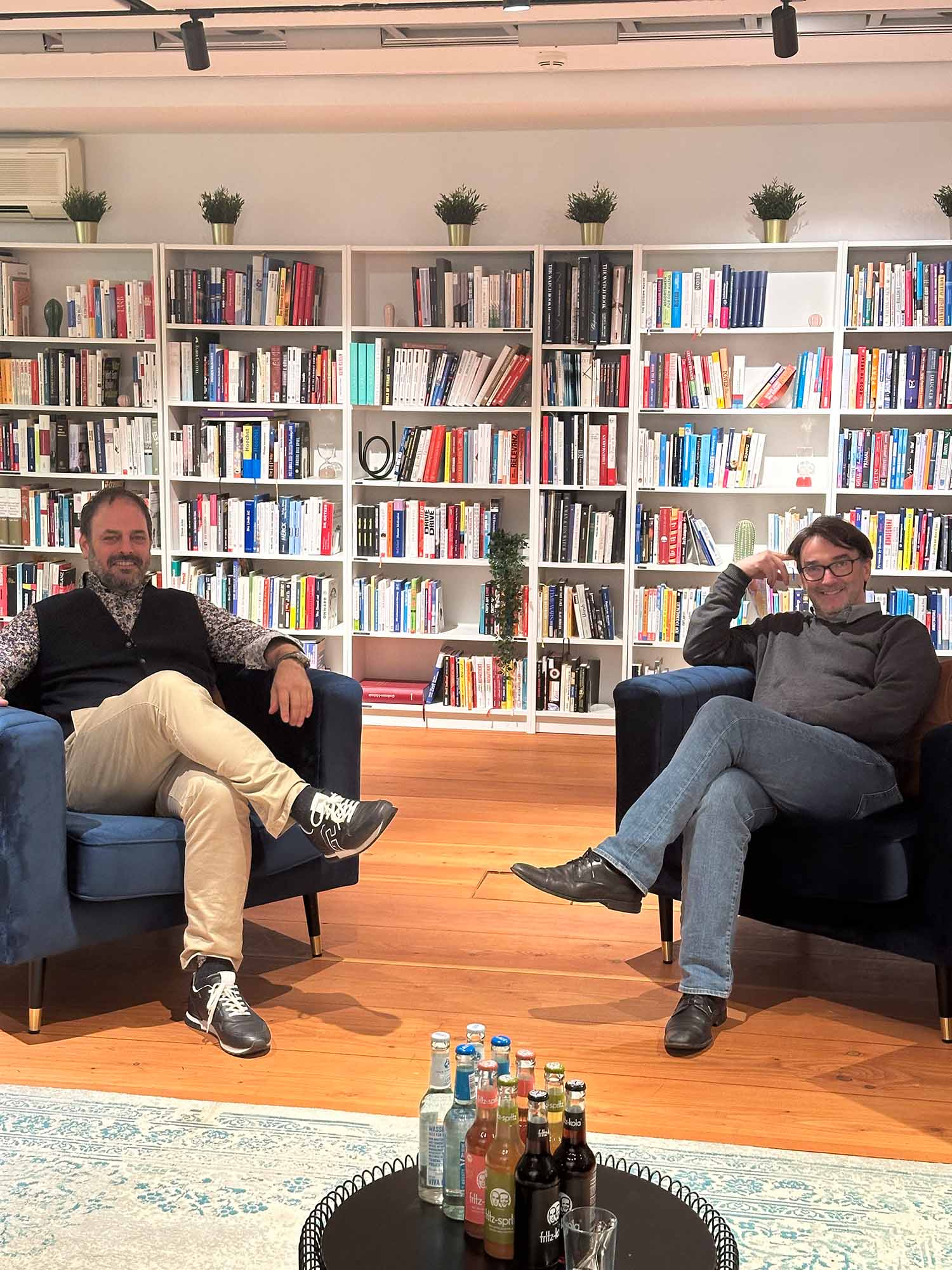 Stefan Grimm und Nikolaus Förster sitzen lächelnd auf zwei großen blauen Sesseln in der Bibiliothek des MachWerks der Bib