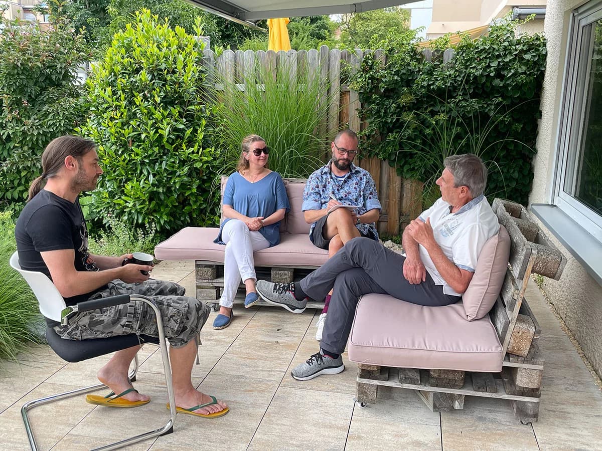 Bodo Grimm im Sommerinterview auf der Terrasse, im Gespräch mit Katja Lafferenz. Sie sitzen auf einer Terasse im Grünen, zwei weitere Personen sind anwesend