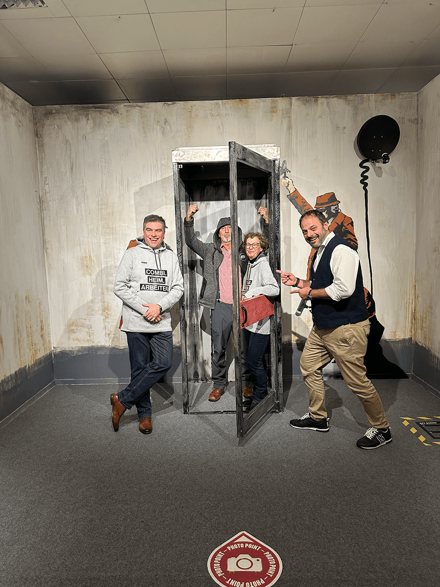 Das CombiTeam bei der Banksy-Ausstellung – mit viel Humor posieren vier Teammitglieder vor einem interaktiven Kunstwerk, darunter eine Telefonzelle und eine Banksy-Graffiti-Figur, die augenzwinkernd die Szene beobachtet.