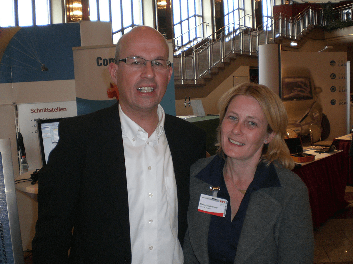 Christian Schmidt und Maren Sundermeyer vom CombiTeam stehen gemeinsam auf einer älteren Messeveranstaltung vor einem CombiSystems-Stand. Im Hintergrund sind Infobanner und Messeausstattung zu sehen – ein Rückblick auf frühere Events.