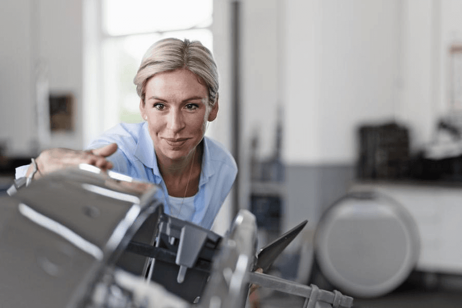 Victoria von Alkewitz inspiziert mit geschultem Blick die Front eines Fahrzeugs in einer Werkstatt. In der Hand ein Tablet, steht sie sinnbildlich für moderne, digitale Schadenbegutachtung in der Kfz-Branche.