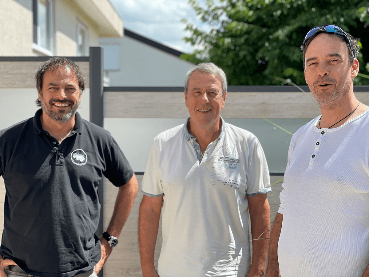 Zwei Generationen CombiSystems: Sebastian, Bodo und Stefan Grimm entspannt im Sonnenschein vor moderner Hausfassade.
