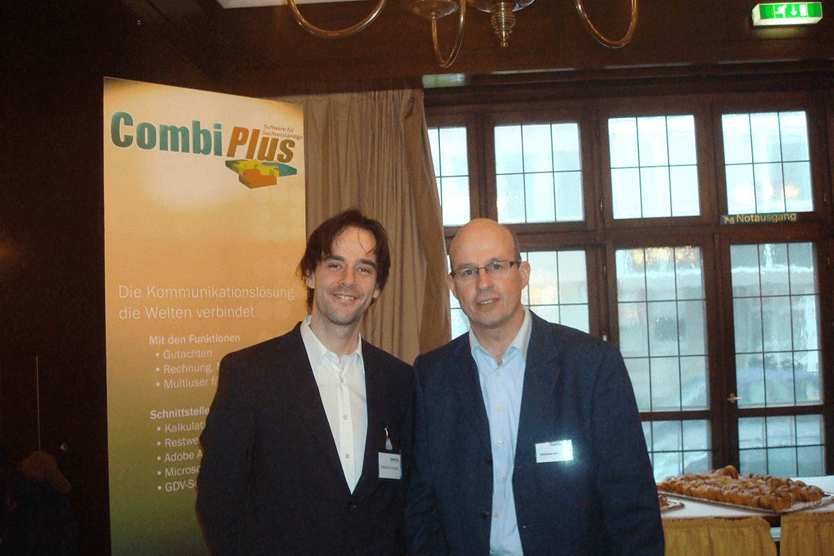 Sebastian Grimm und Christian Schmidt bei einem früheren CombiPlus-Messeauftritt, elegant gekleidet vor einem Roll-up mit CombiProduktinformationen.
