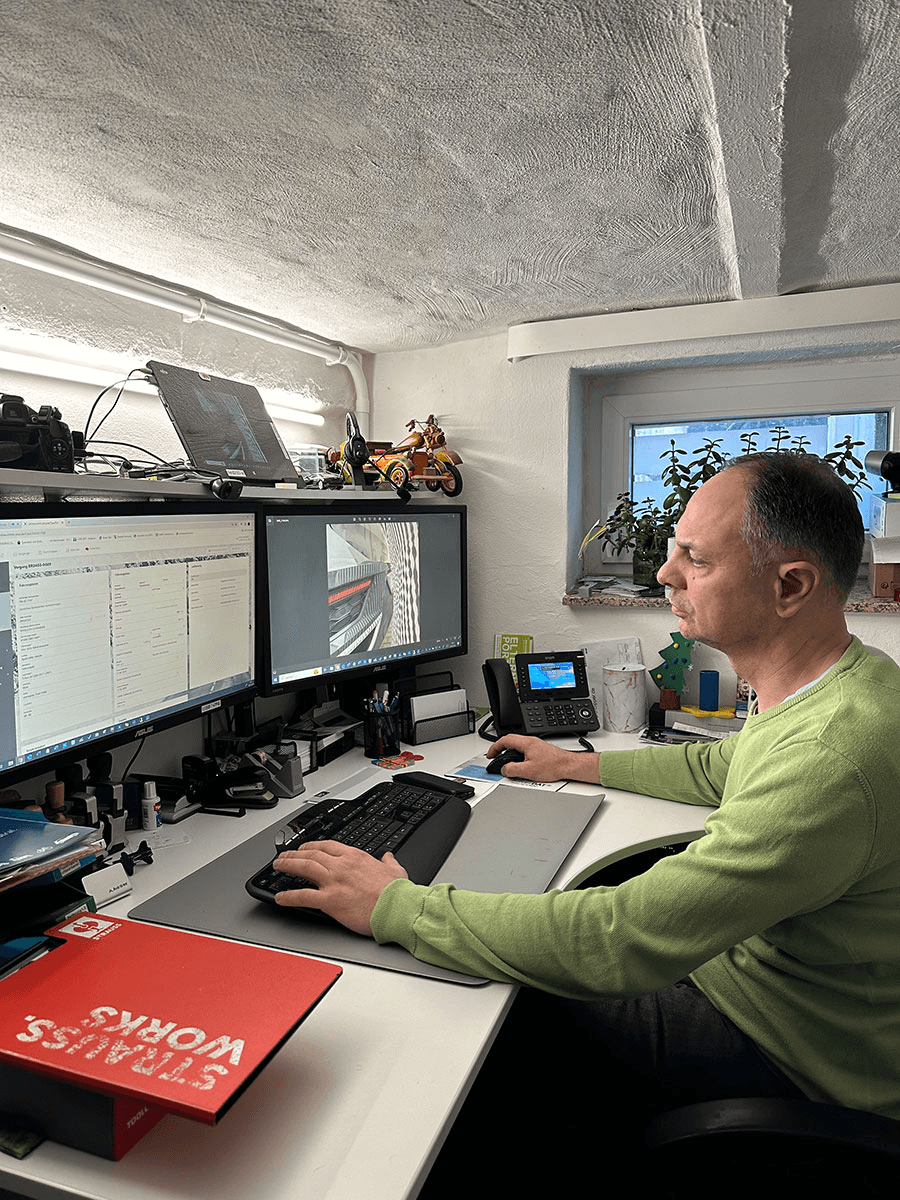 Enrico Rehberg, ein CombiKunde, arbeitet konzentriert an einem Schreibtisch mit zwei Monitoren. Auf den Bildschirmen sind Schadenfotos und Eingabemasken eines digitalen Kfz-Schadenmanagementsystems zu sehen – ein moderner Arbeitsplatz im Sachverständigenwesen.
