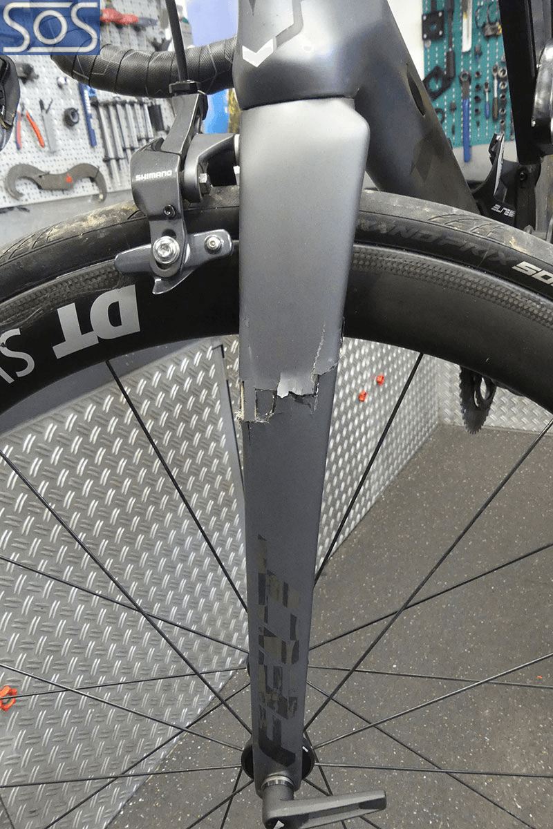 Nahaufnahme einer beschädigten Carbon-Gabel eines Rennrads mit einem deutlich sichtbaren Riss und abgeplatztem Material – aufgenommen in einer Fahrradwerkstatt.