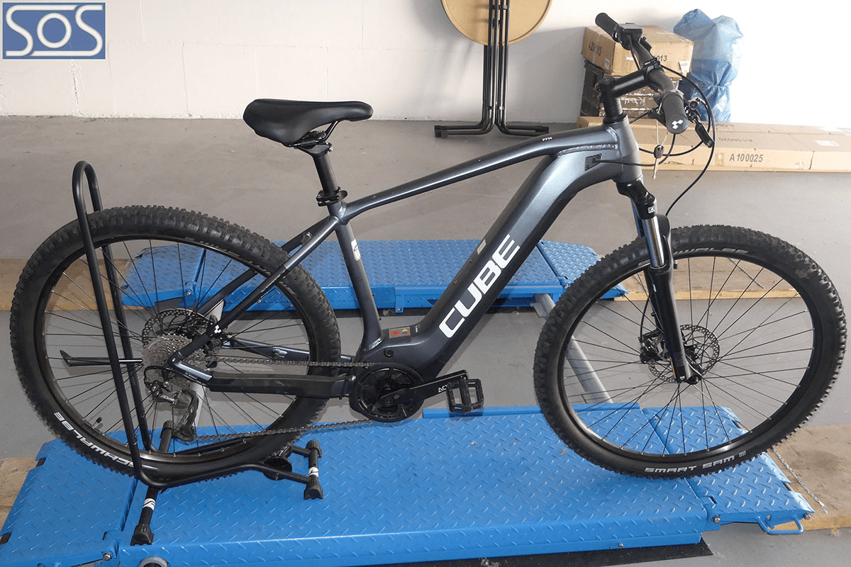 Ein graues E-Bike der Marke CUBE steht auf einer blauen Werkbank in einer Werkstatt – das Fahrrad ist vollständig montiert und wird von einem Ständer an Ort und Stelle gehalten.