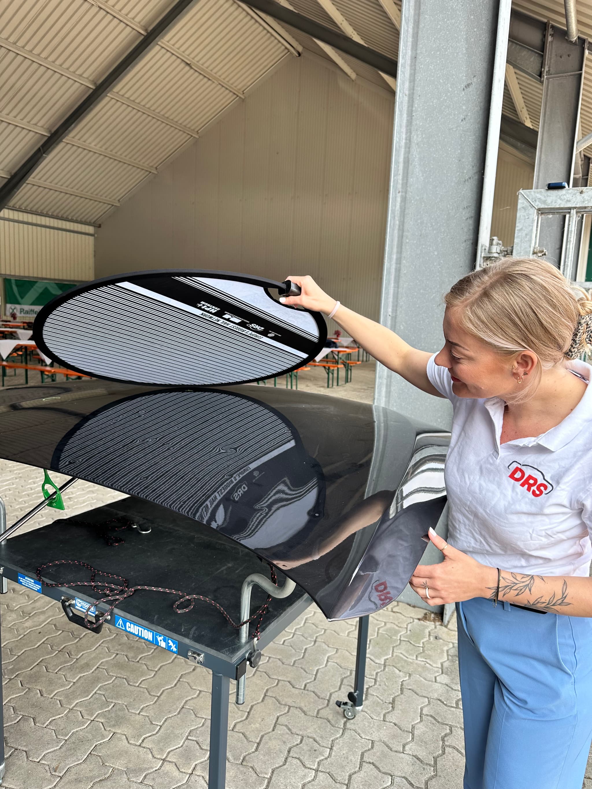 Eine DRS-Expertin demonstriert beim LeeseDay den Einsatz eines Spiegelboards zur Erkennung von Dellen an einer Fahrzeugmotorhaube – praxisnah und präzise.