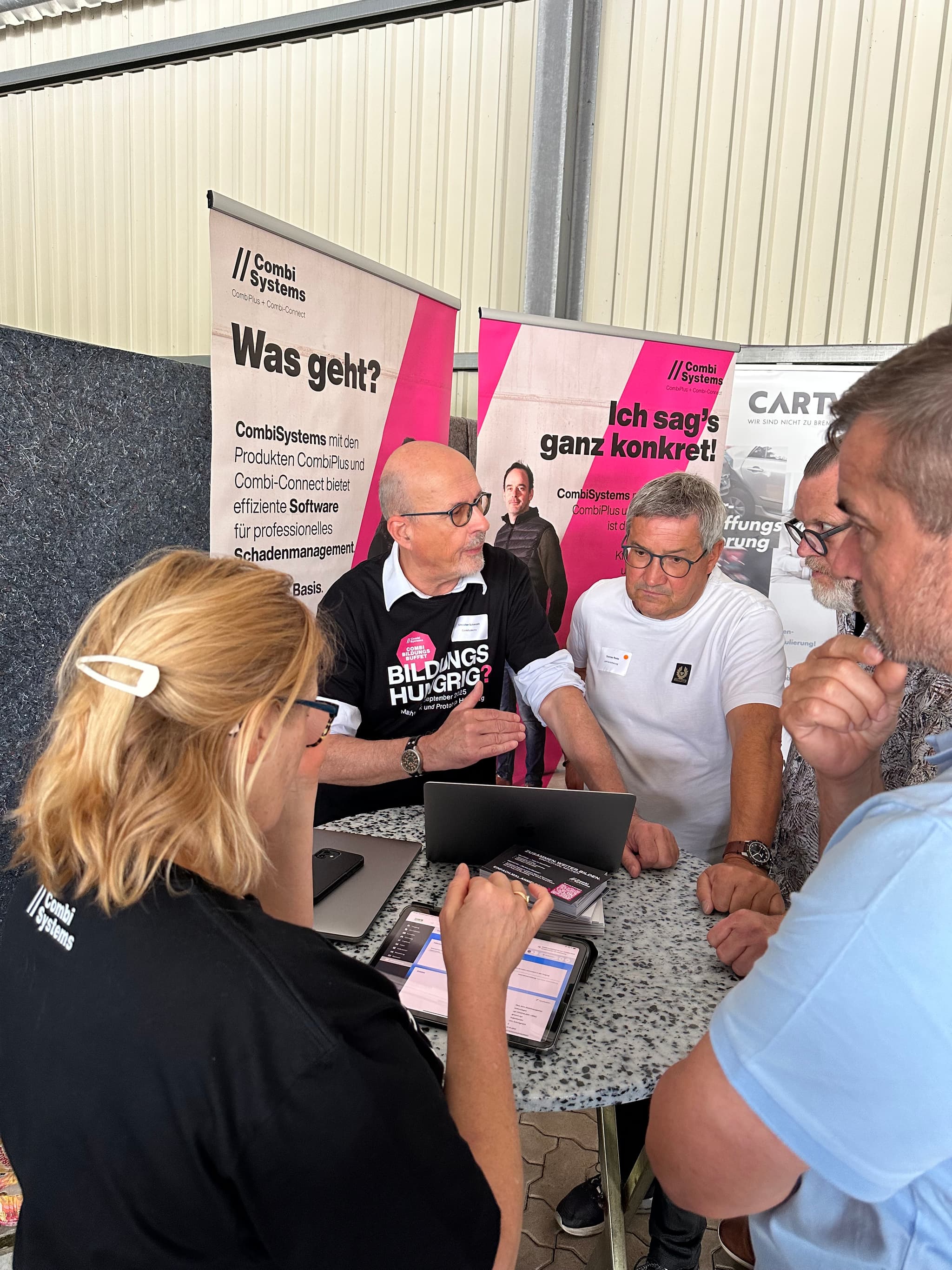 Auf dem Bild sind Maren Sundermeyer und Christian Schmidt vom CombiTeam zu sehen. Sie stehen beim LeeseDay im Austausch mit Interessierten und tragen dabei ihre schwarzen CombiBildungsBuffet Shirts mit dem auffälligen pinken Aufdruck "Bildungshungrig?".