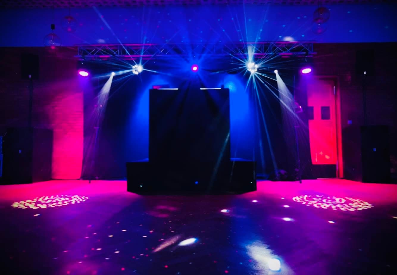 Leere Tanzfläche mit spektakulärer Lichtshow in Magenta und Blau, vorbereitet für einen Auftritt von DJ Chicken Beats.