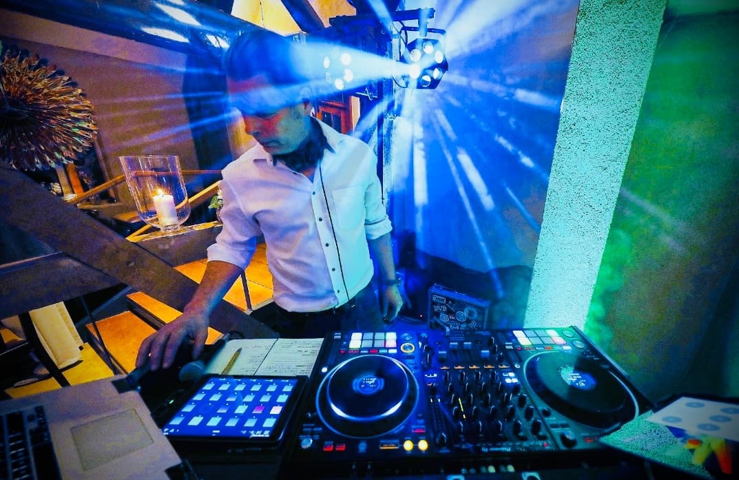DJ Chicken Beats im Einsatz an seinem DJ-Pult, fokussiert bei der Arbeit, umgeben von Lichteffekten und Technik.