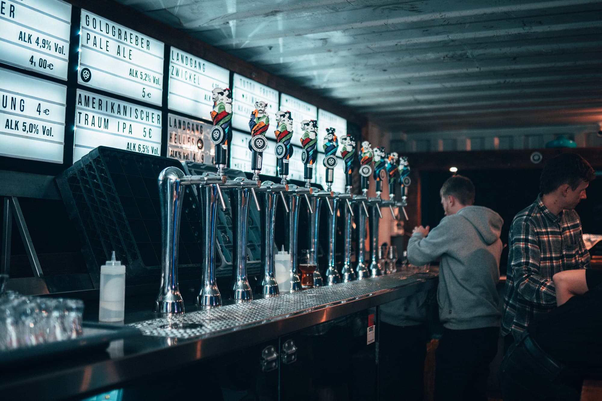 Langer Tresen mit zahlreichen Zapfhähnen und beleuchtetem Biersortiment in der Landgang Brauerei; Gäste lassen sich Getränke einschenken.