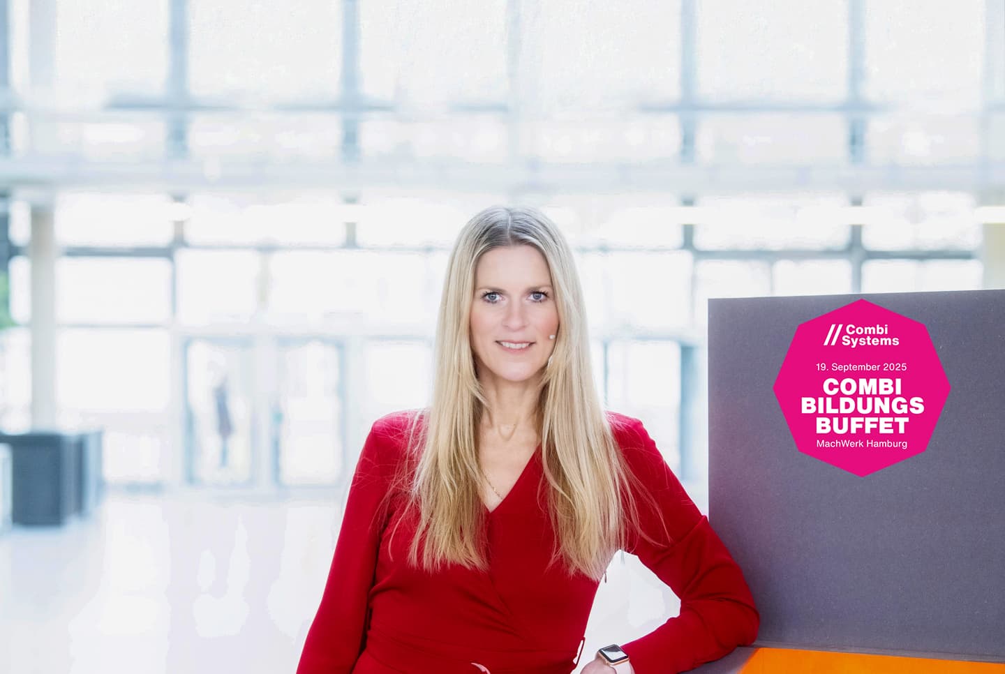 Porträt von Silke Leinweber, Moderatorin beim CombiBildungsbuffet 2025.Sie trägt ein rotes Kleid und befindet sich in einer Ausstellungshalle, gelehnt an ein Pult.